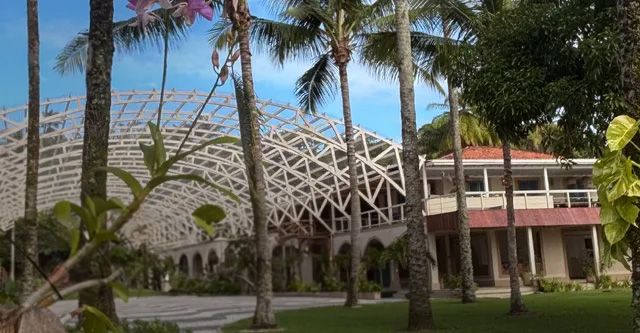 Tropical resort with white latticework roof, two-story building, and palm trees. Text: 