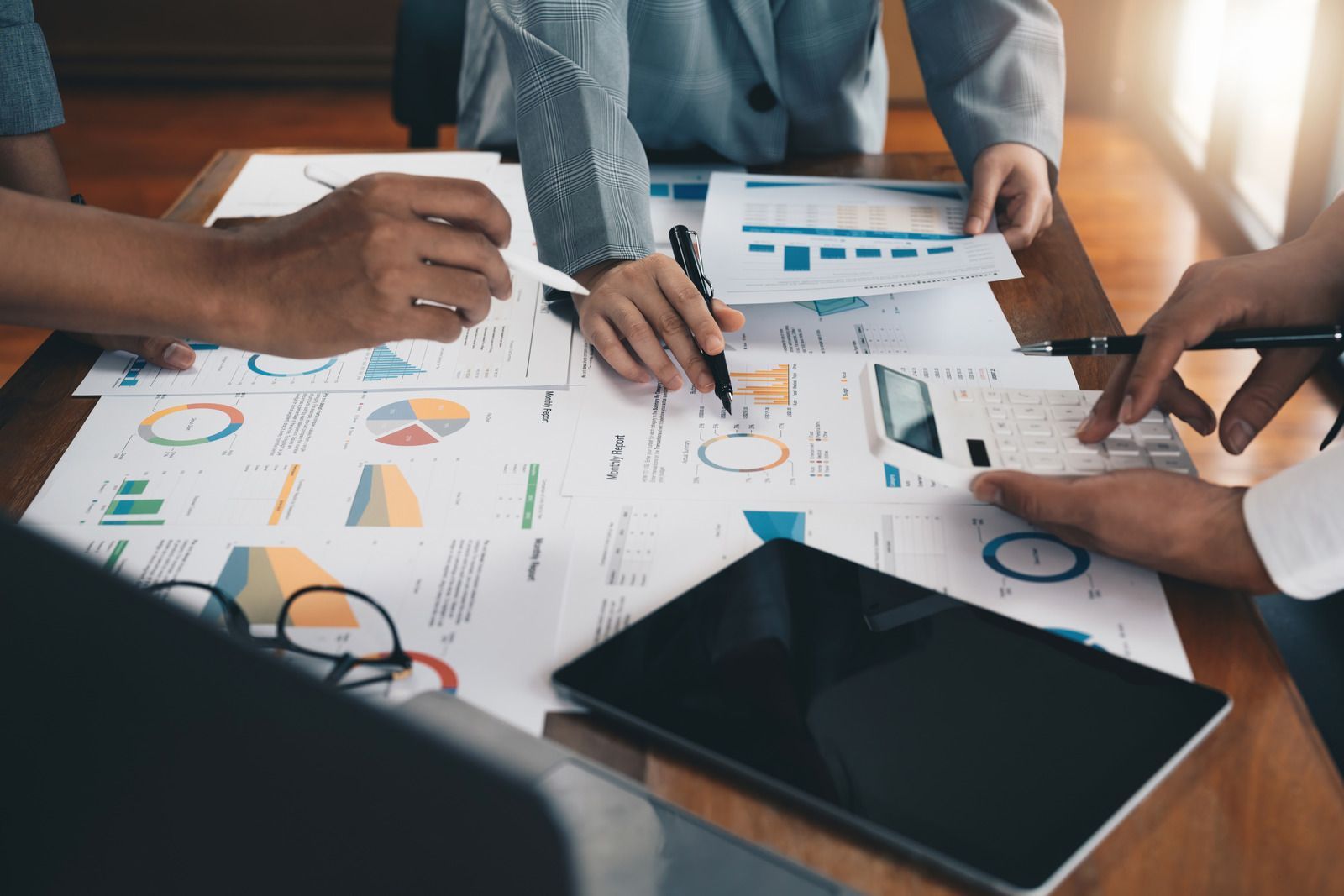 Two people analyzing stock market data on a laptop and tablet, pointing at graphs with rising and falling trends.