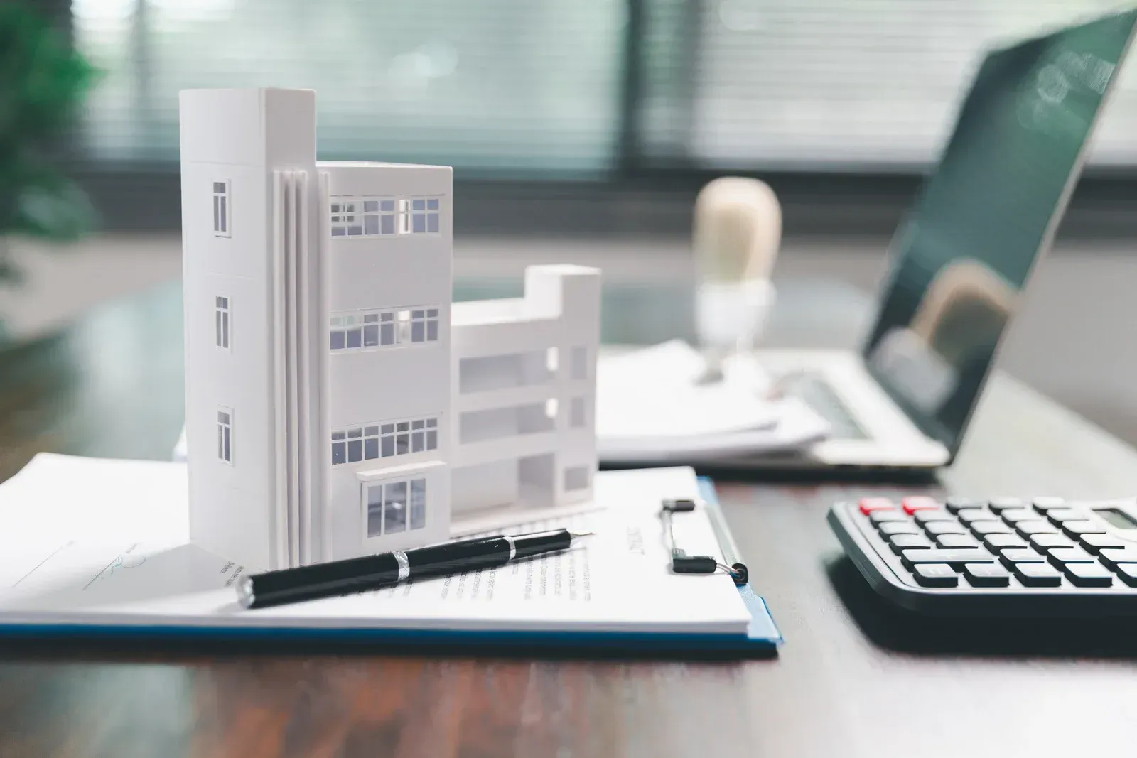 Model building on paperwork with pen, laptop, and calculator, suggesting real estate or financial planning.