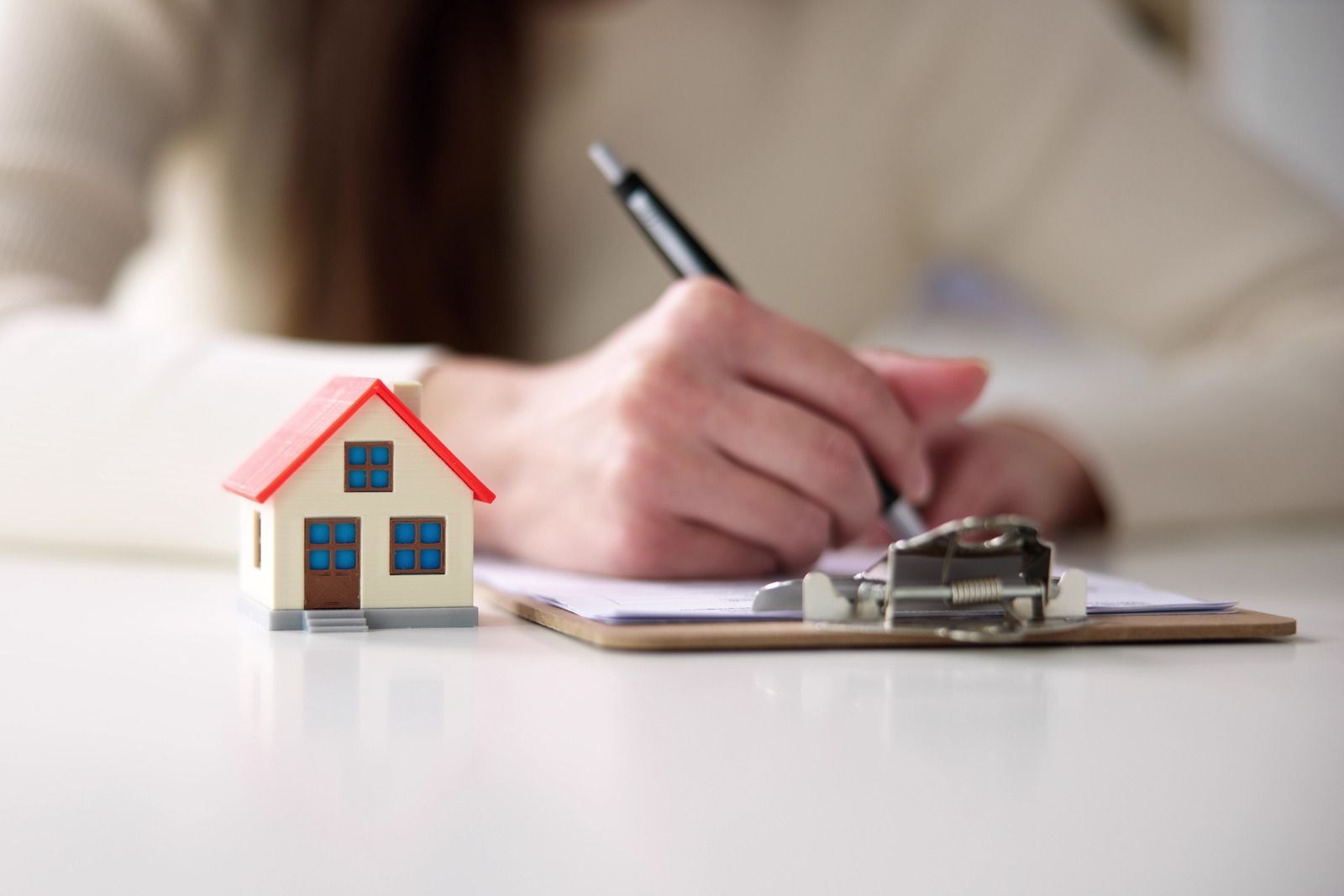 Toy house next to a person writing on a clipboard, possibly a real estate transaction.