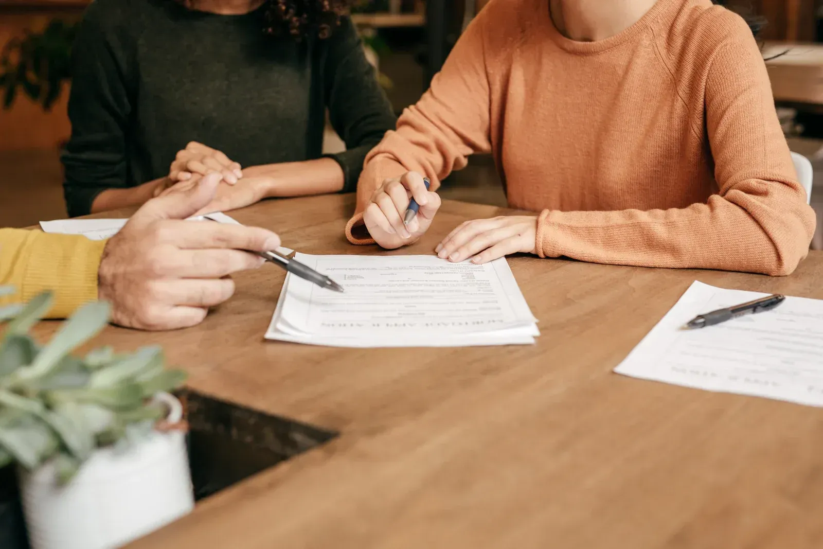 People at table review documents; one points while others hold pens.