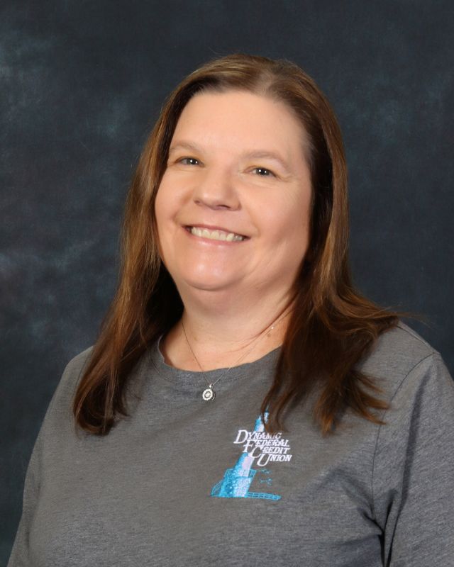 Woman in gray shirt, smiling, with logo on the chest. Against a blue background.