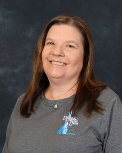Woman in gray shirt, smiling, with logo on the chest. Against a blue background.