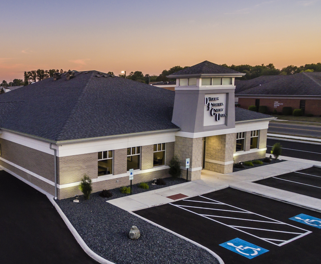 Dynamic Federal Credit Union building, exterior view; gray, brick, and stone facade; blue sky.