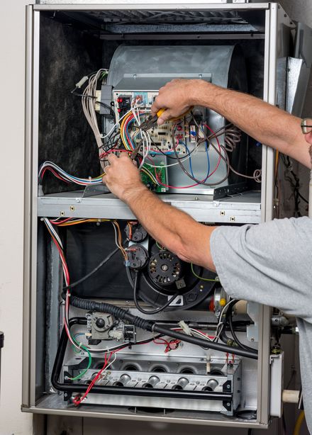 Person working on a furnace's electrical components; wires and circuit boards are visible.