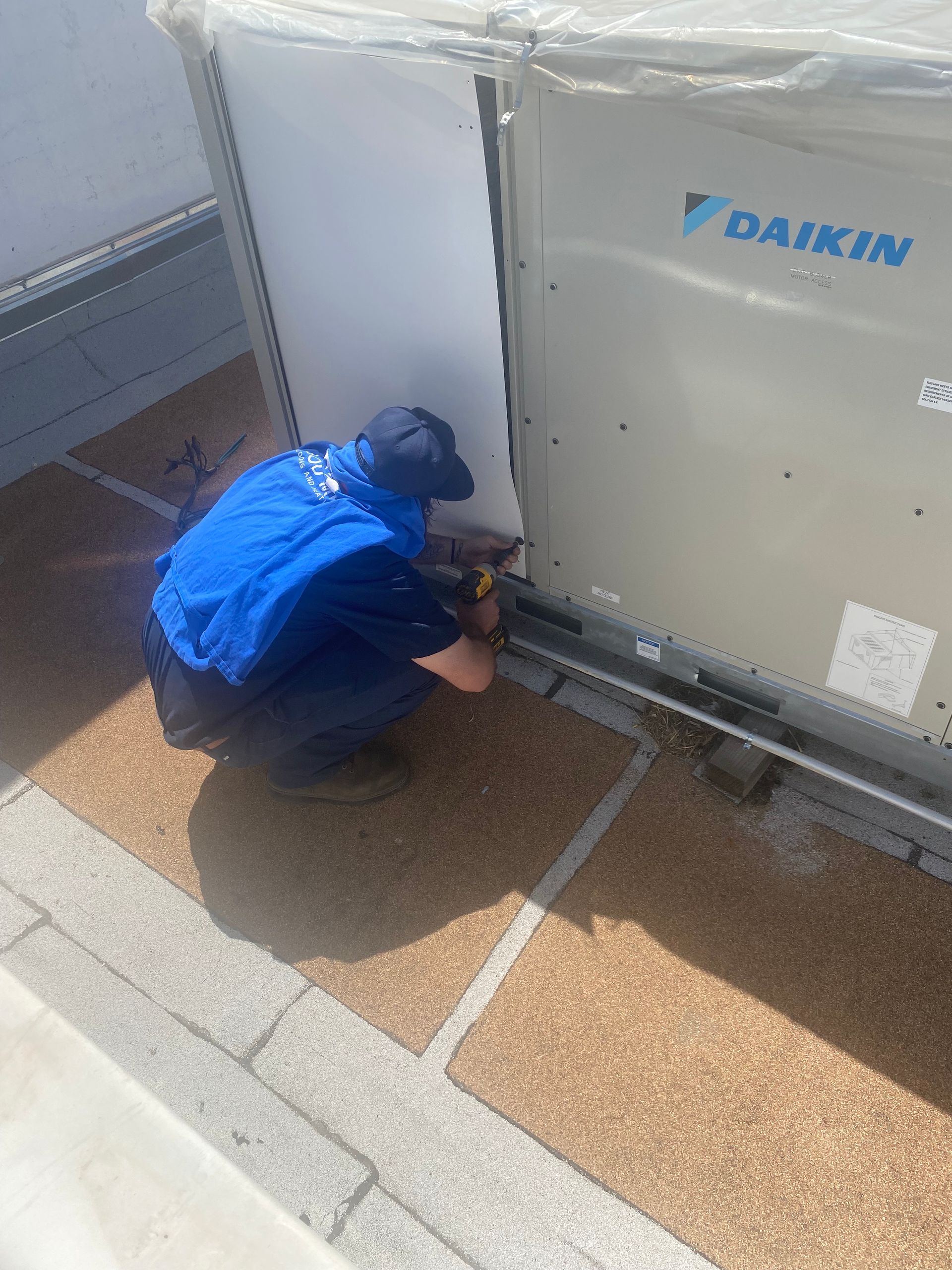 A man in a blue jacket is working on a daikin air conditioner.