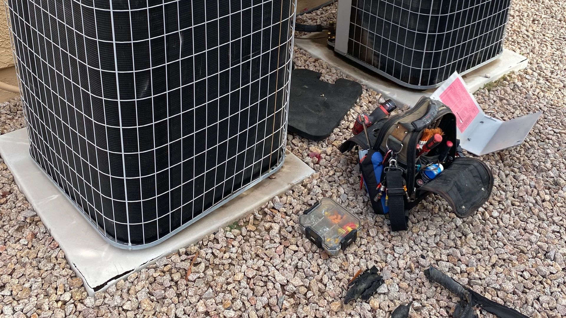 A couple of air conditioners sitting on top of a gravel floor.