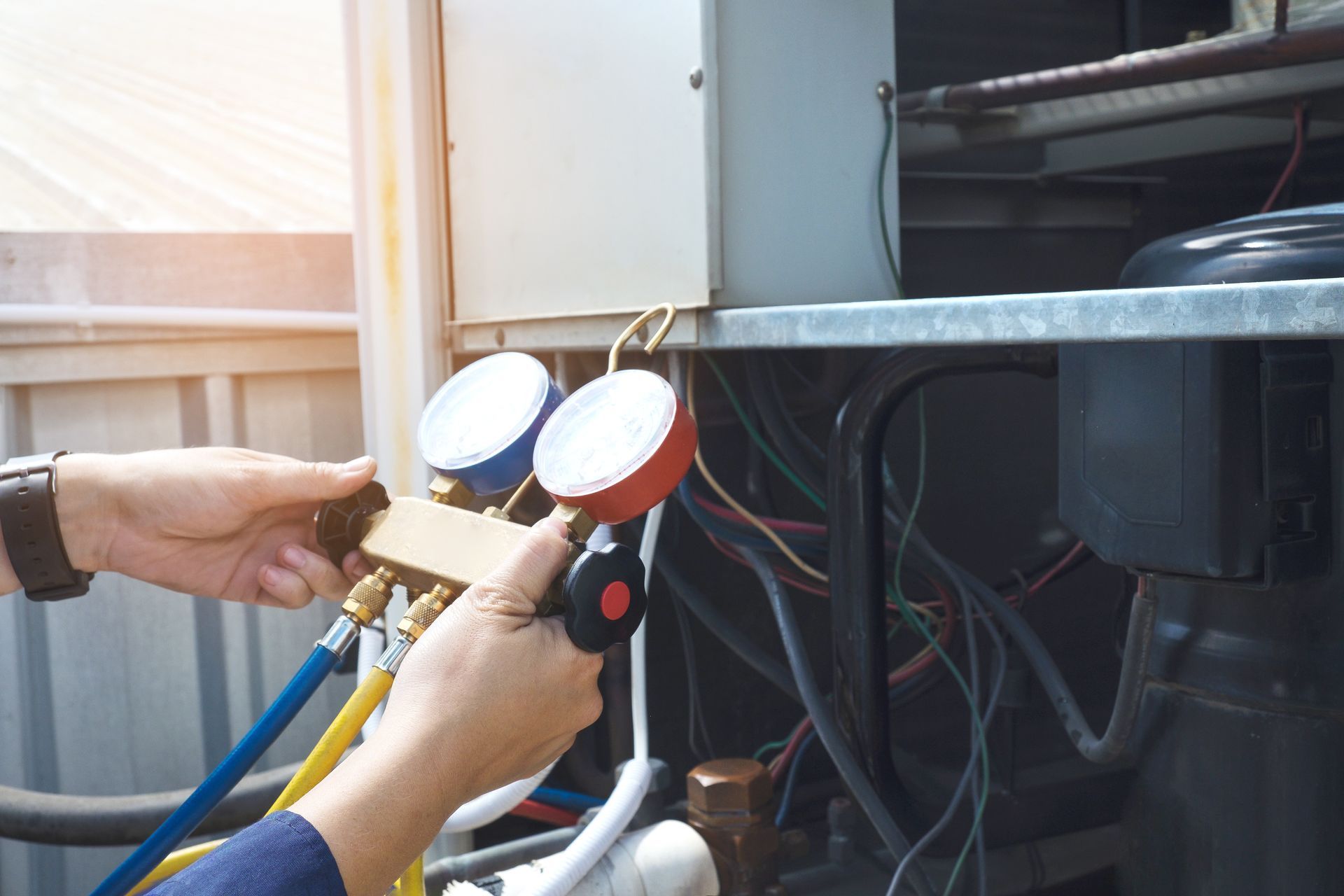 A technician holds a colorful HVAC manifold gauge set while servicing an outdoor air conditioning unit.