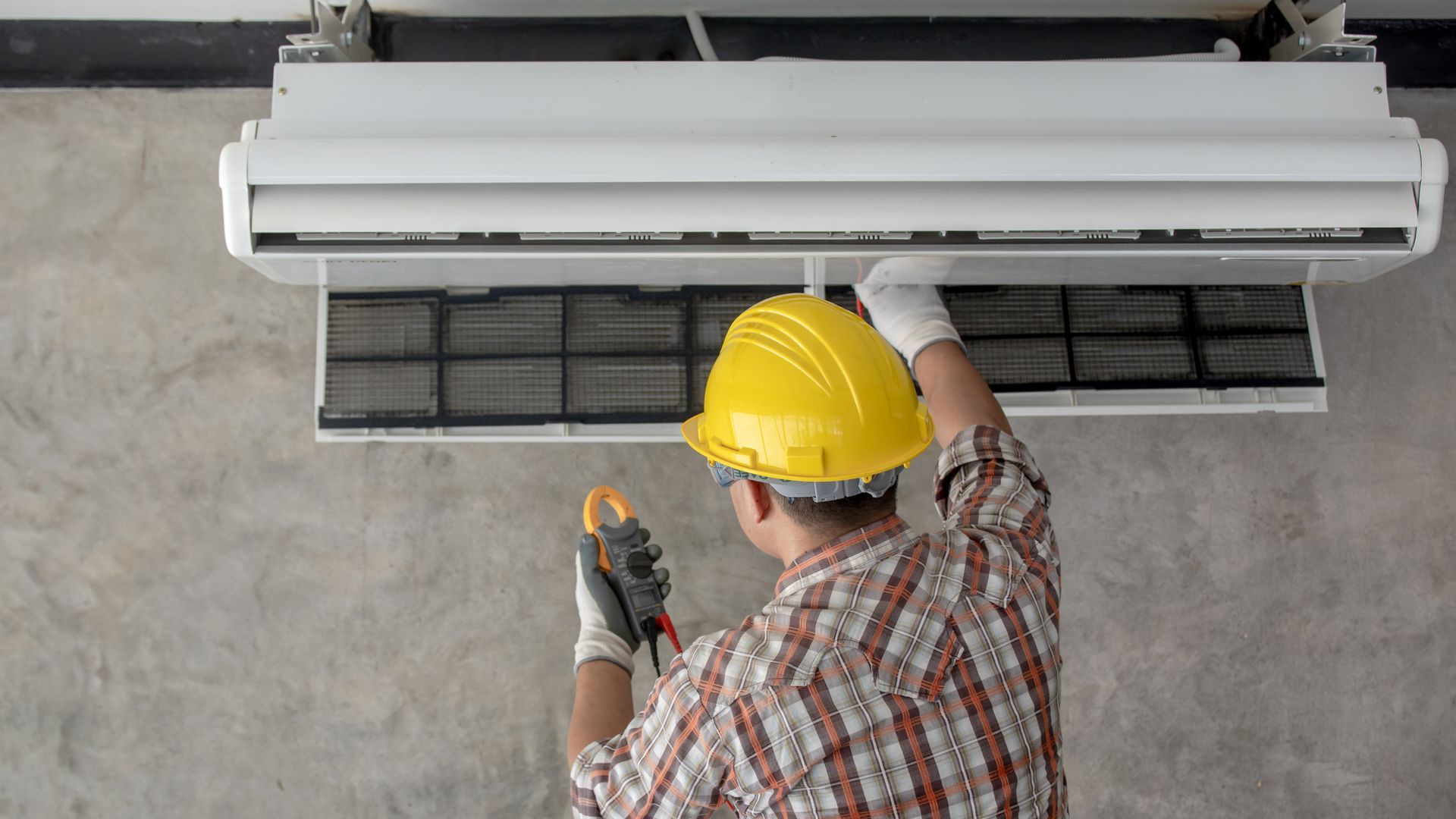 A man wearing a hard hat is working on an air conditioner.