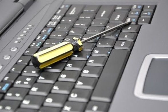 Black HP or Microsoft Laptop with a yellow screw driver used for repair sitting on the black keyboard