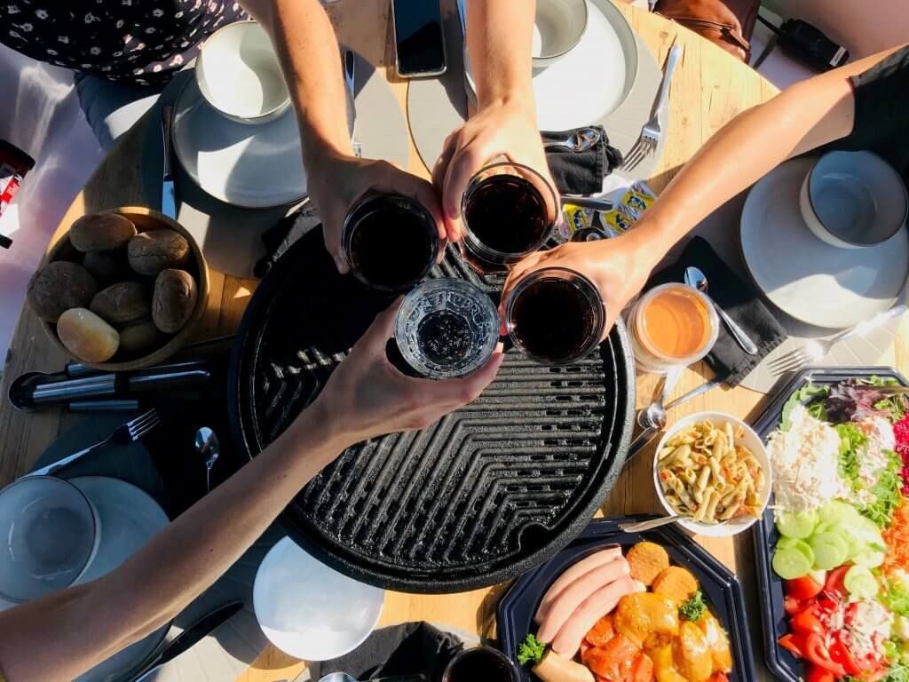 Vrienden proosten met drankjes rond een barbecue, terwijl ze genieten van schalen vol eten en salades op een boot