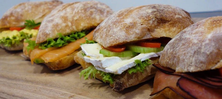Diverse knapperige sandwiches op een houten plank, gevuld met sla, tomaat en vlees.
