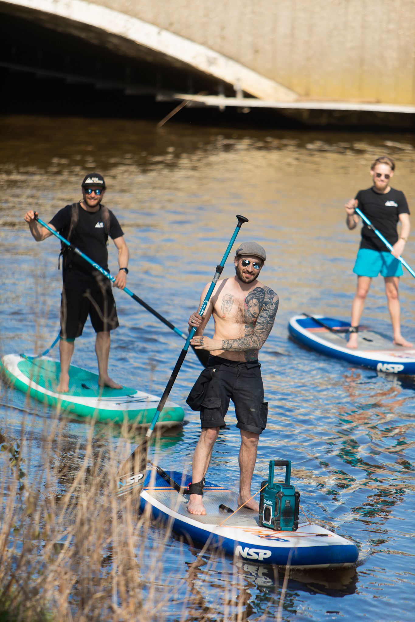 Drie mannen staan ​​op paddleboards in het water.