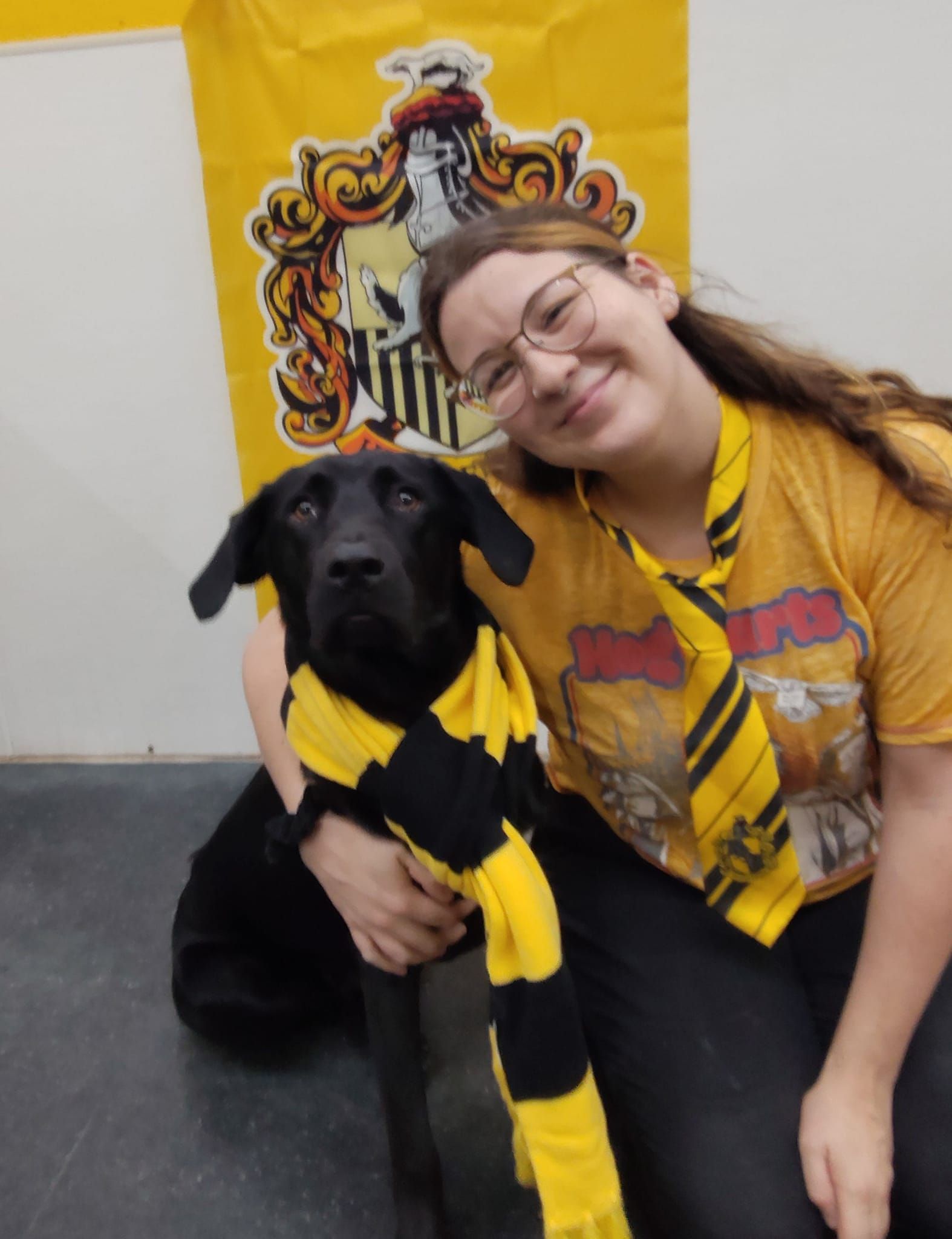 A woman and a black dog are posing for a picture in front of a hufflepuff flag