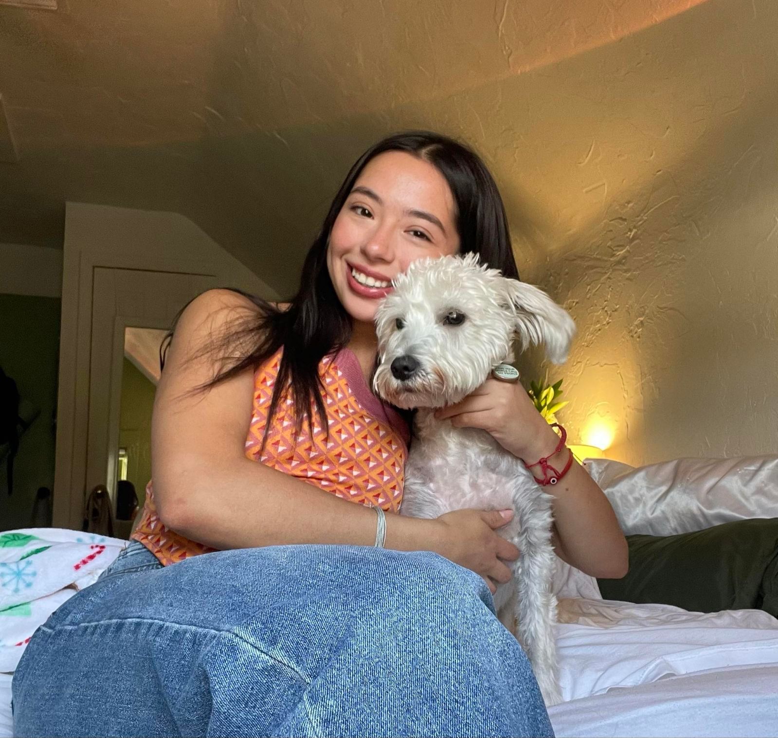 A woman is sitting on a bed holding a small white dog.