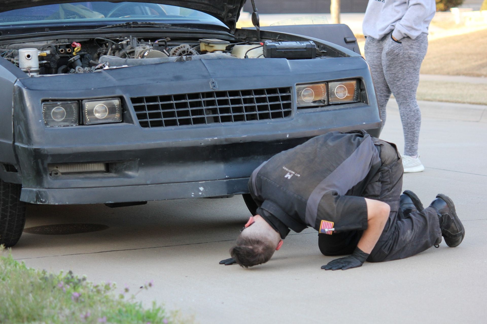 A man is kneeling down under the hood of a car.