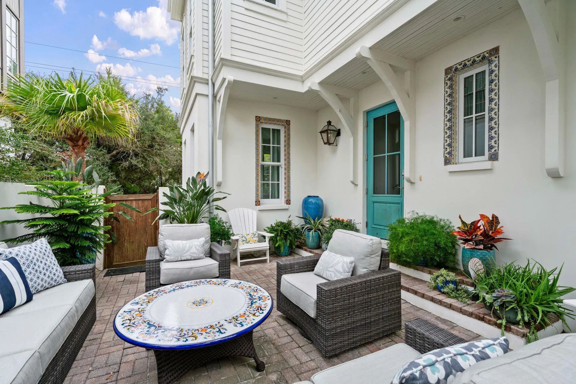 Outdoor patio with seating, colorful table, teal door, and lush plants.