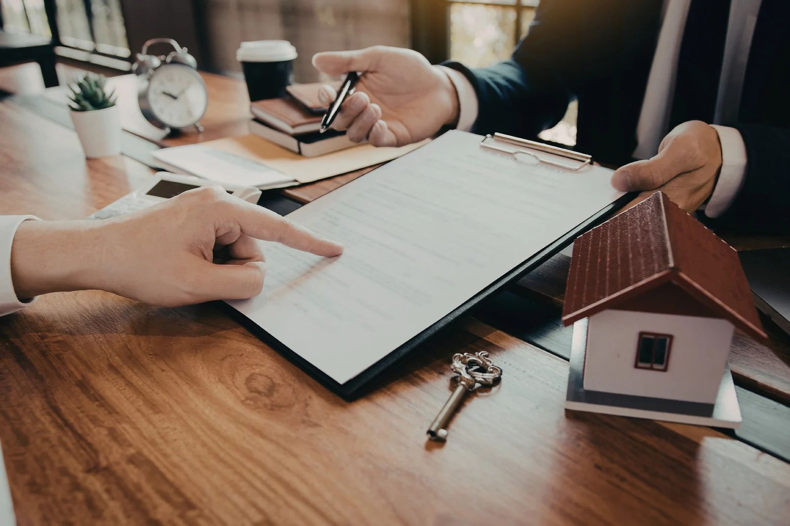 Two people reviewing a real estate contract at a desk with a small house model and a key.