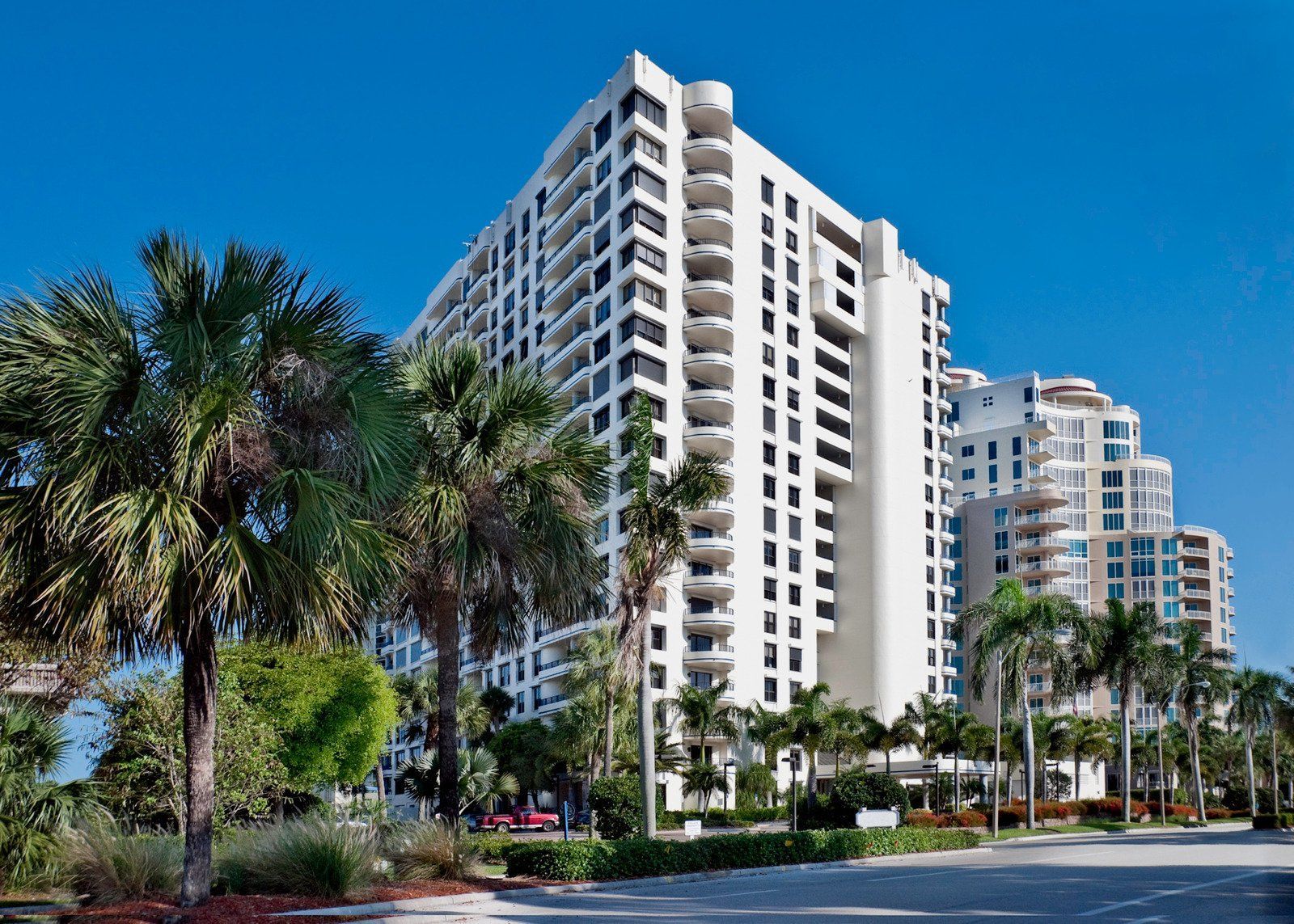 White high-rise building with balconies, palm trees in front, clear blue sky.