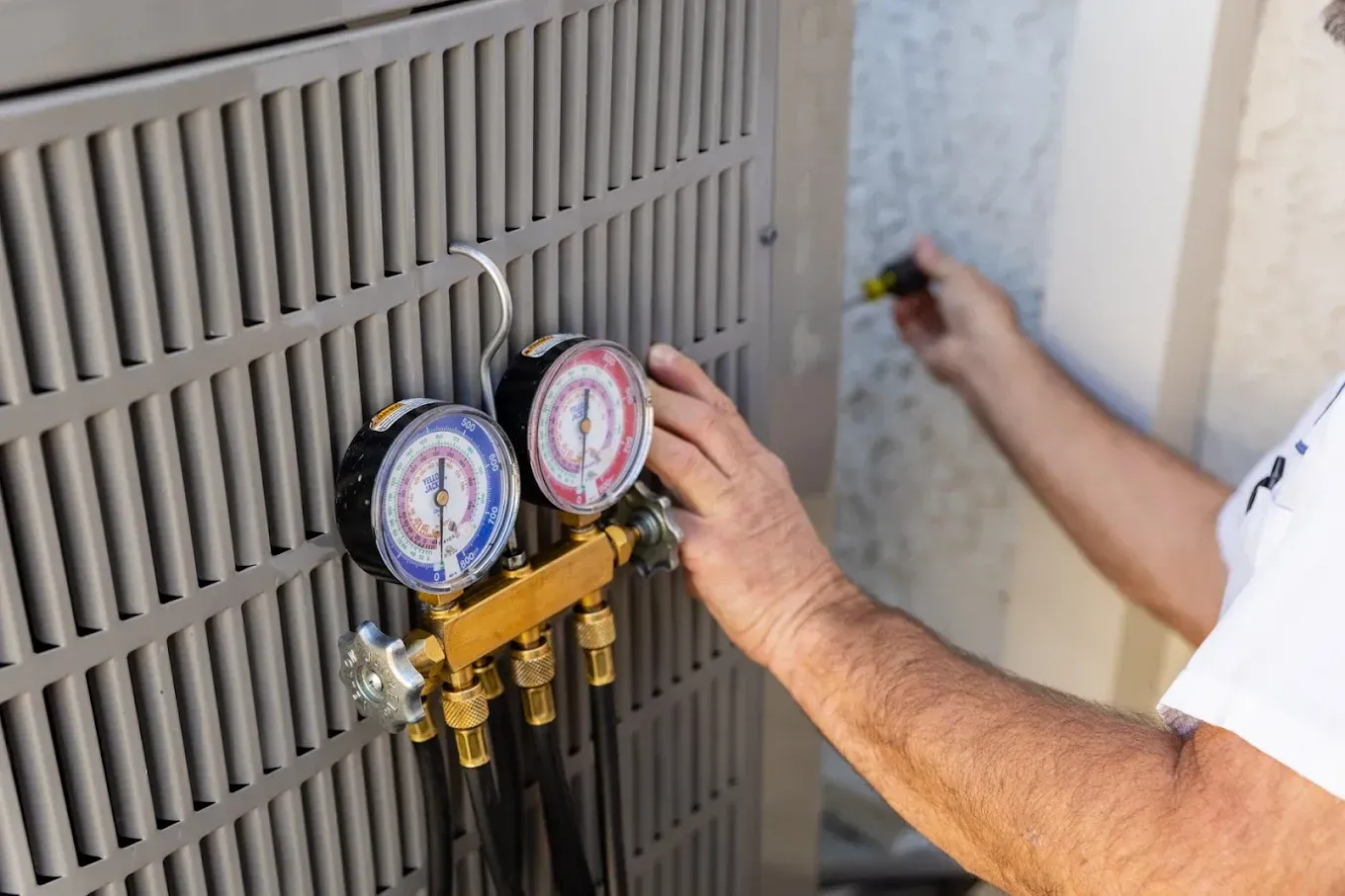 HVAC technician working on an outdoor AC unit; gauges and tools are visible.