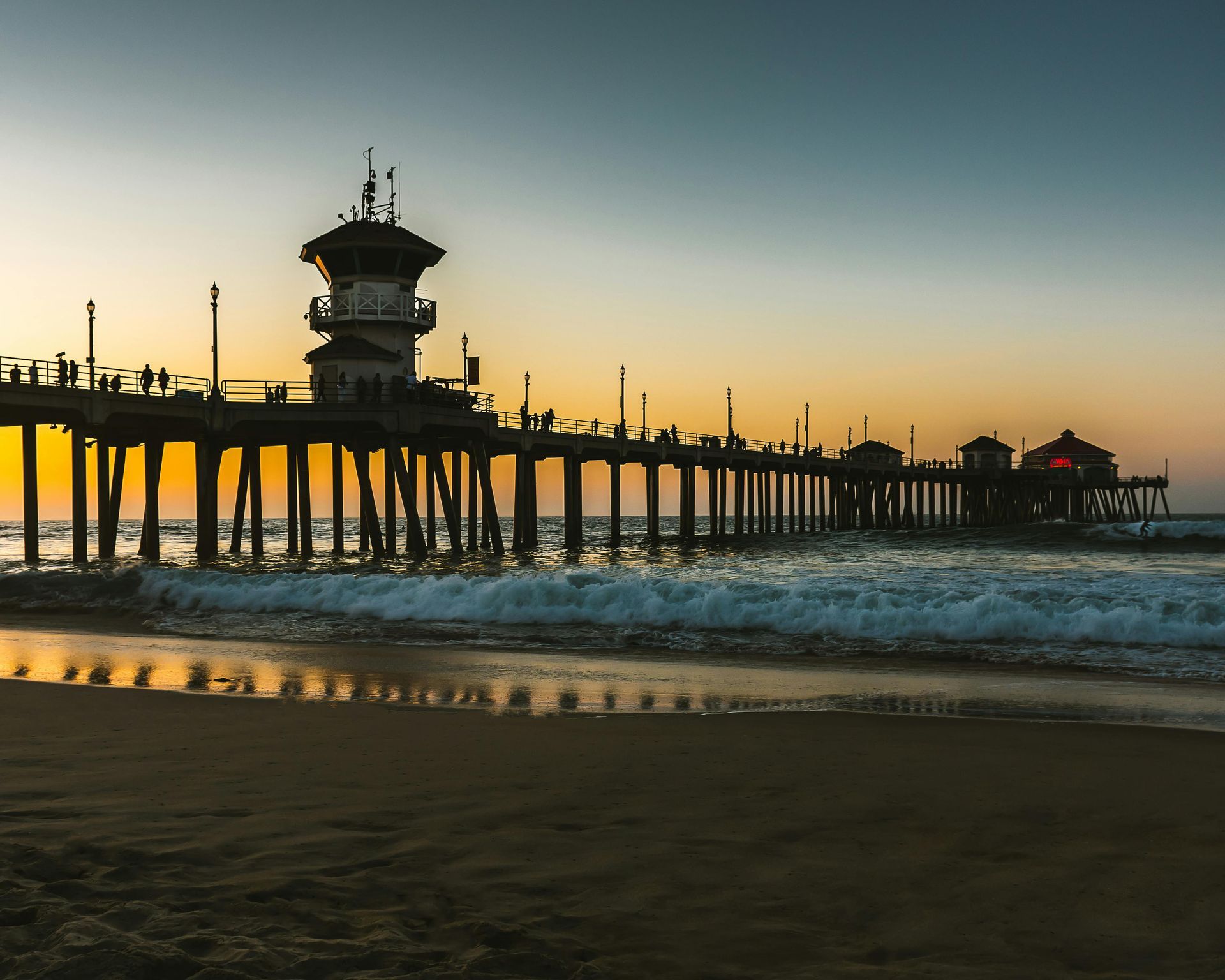 Pier at sunset with silhouetted structures against the colorful sky, waves crashing on the shore.