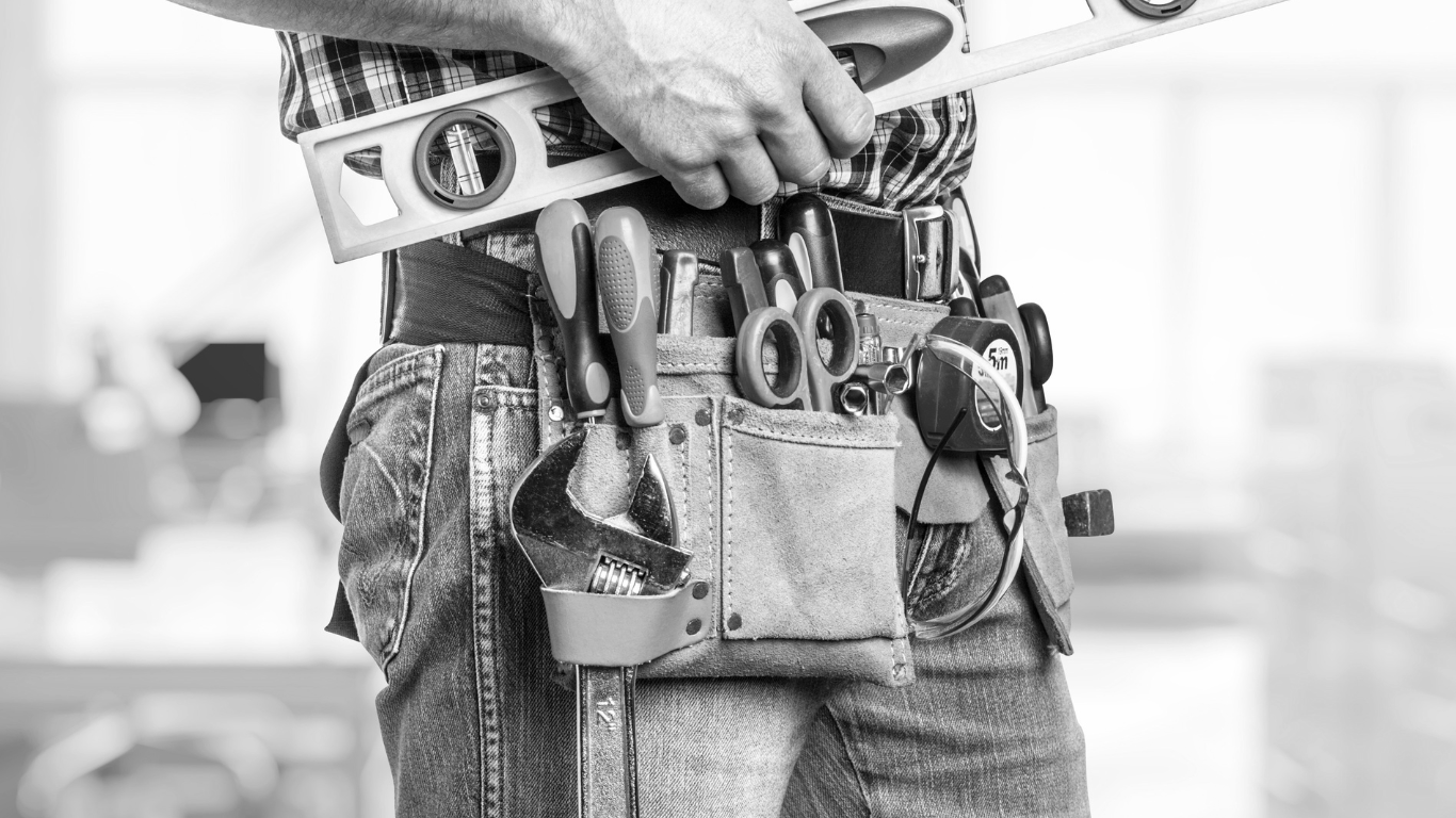 A man is wearing a tool belt and holding a level.