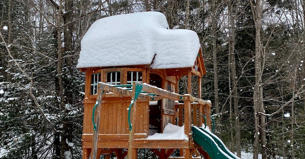 A wooden playset with a slide and a tree house covered in snow.