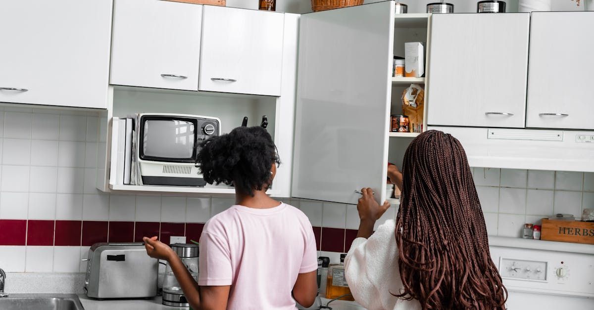 Two women are standing in a kitchen looking in a cabinet.