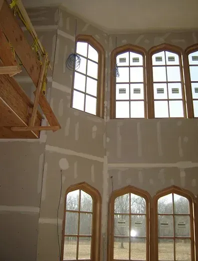 Interior view of a building under construction, featuring arched windows and drywall.