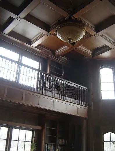 Wooden paneled library with balcony, windows, and ornate ceiling fixture.