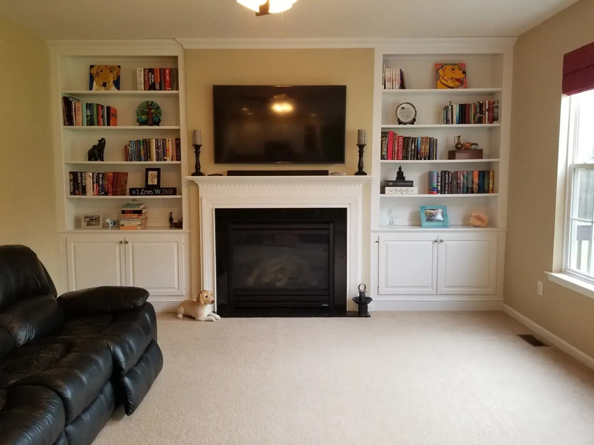 Living room with built-in bookshelves flanking a fireplace and TV. A dog lounges on the carpet near a black leather sofa.