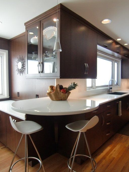 Modern kitchen with dark wood cabinets, white countertops, and bar stools.