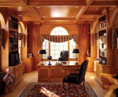 Wooden paneled home office with desk, bookshelves, and arched window.