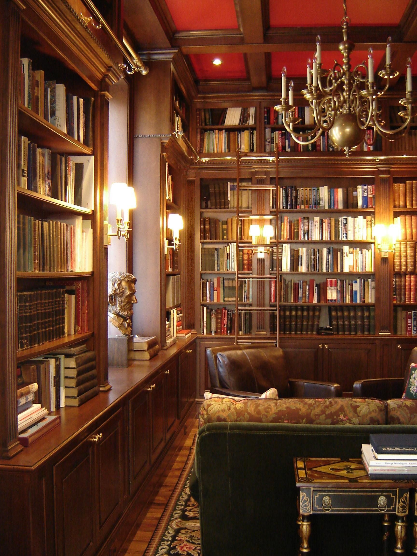 A cozy library with dark wood shelves filled with books, a rolling ladder, and a green velvet sofa.