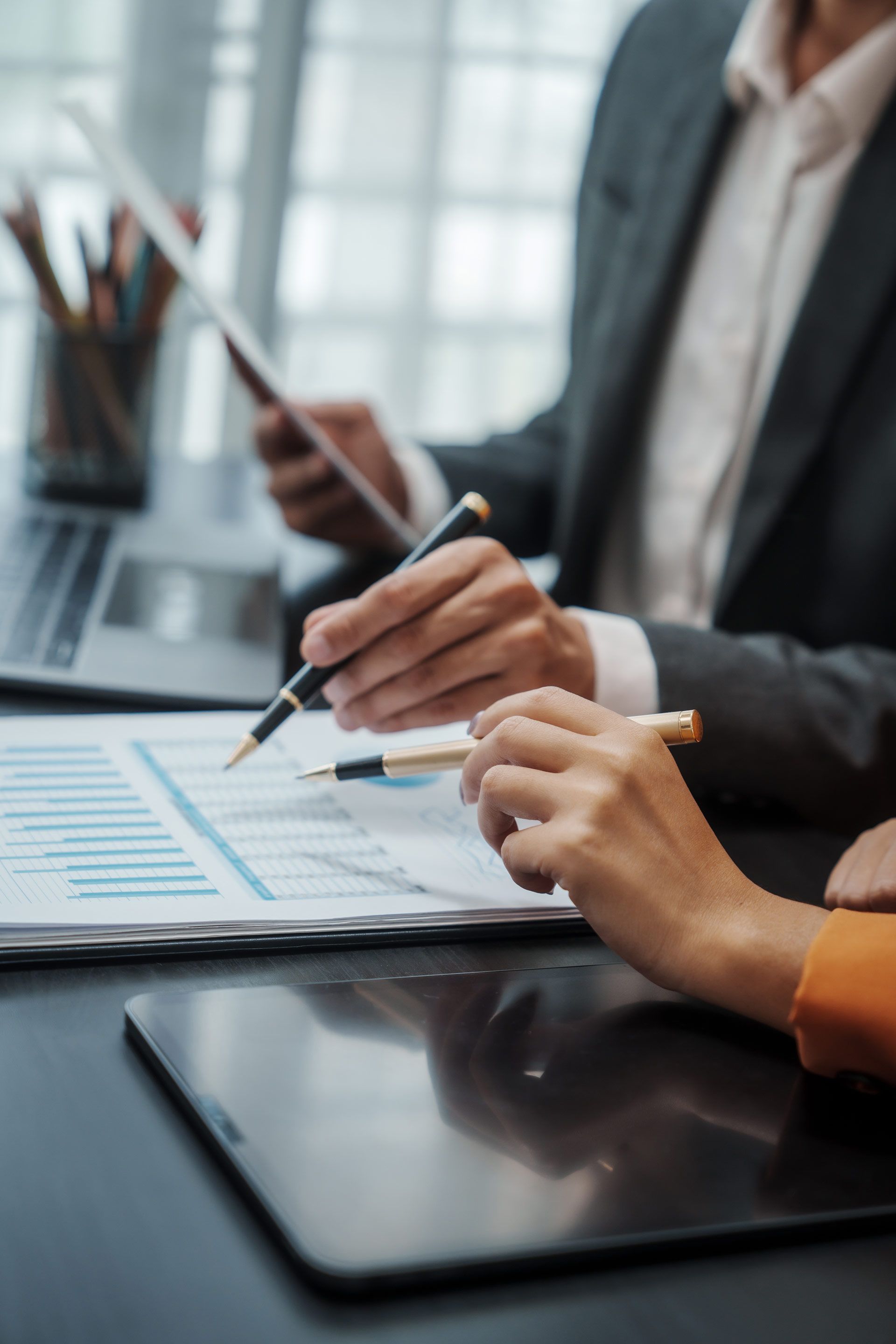 Two people reviewing charts, pointing with pens. One wears a suit jacket.