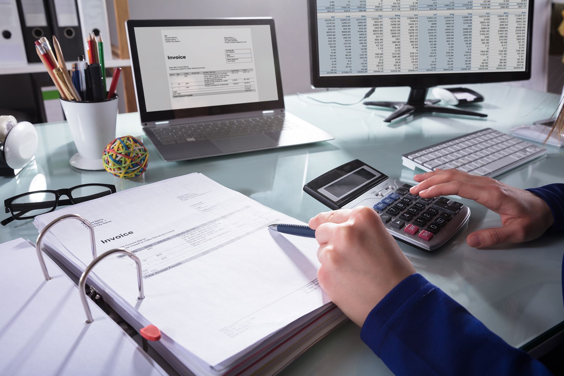 Person using a calculator and laptop, working on financial documents at a desk.