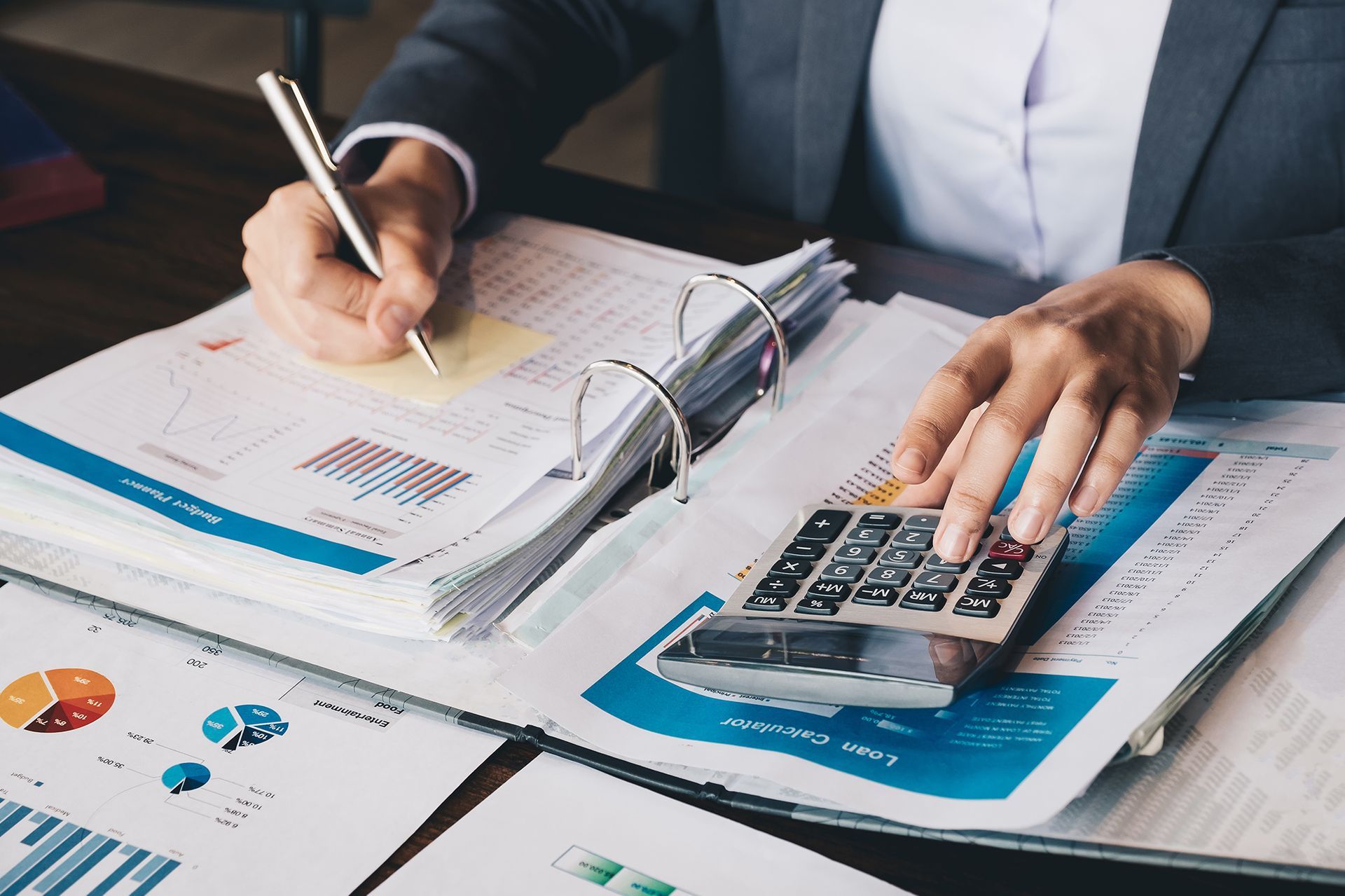 Person in suit uses calculator while reviewing documents.