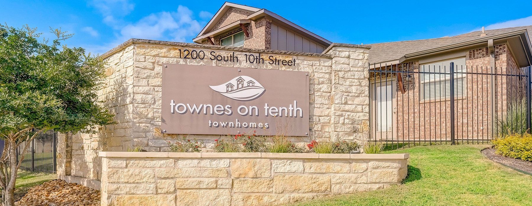 Exterior stone entrance sign for Townes on Tenth townhomes with landscaping.