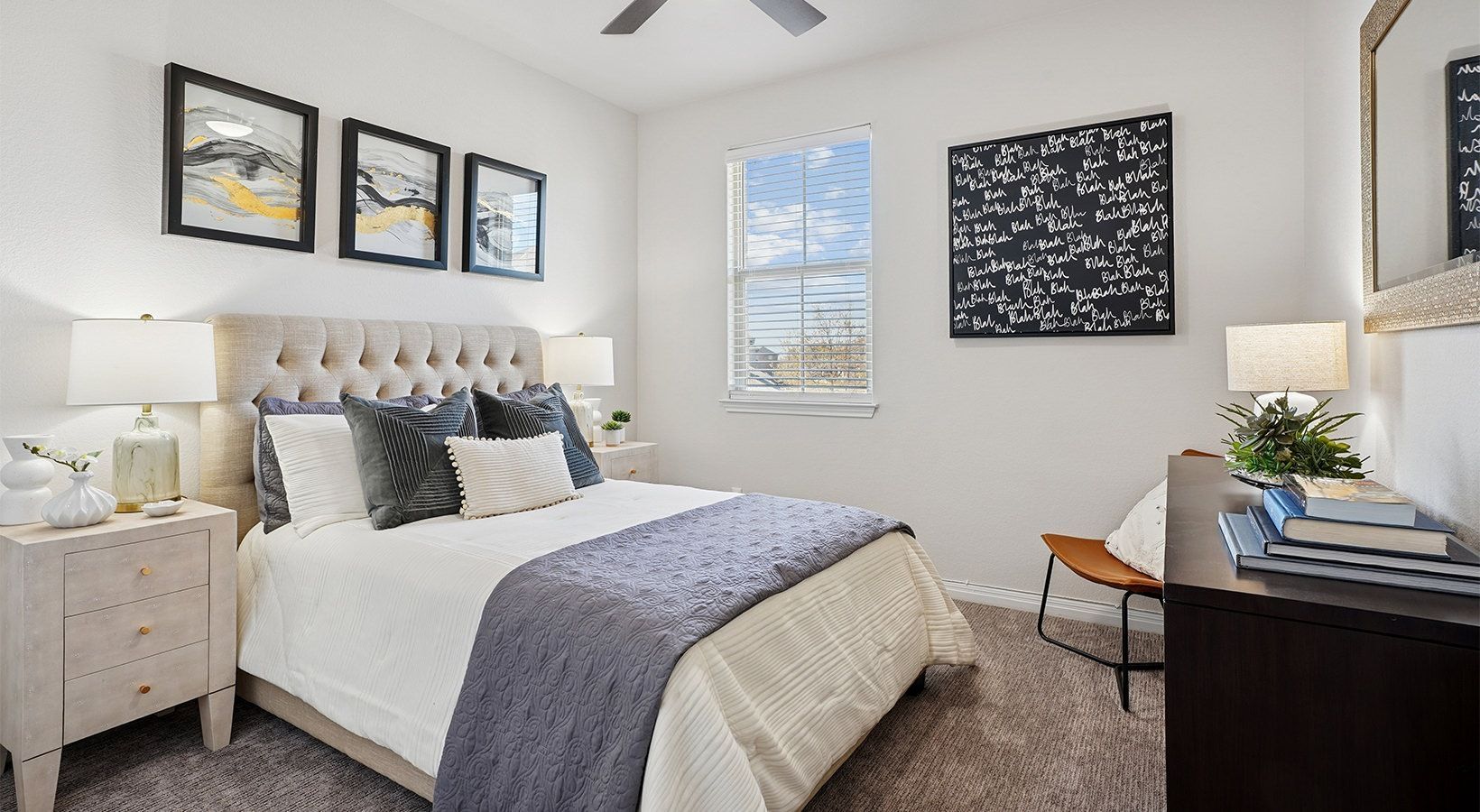 Bedroom in a modern apartment with tufted headboard, two nightstands, lamps, and a desk.