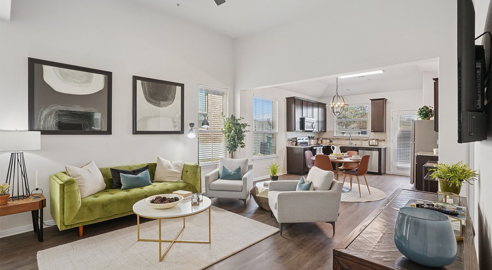 Open-plan living area with green sofa, two gray chairs, coffee table, and a kitchen in the background.