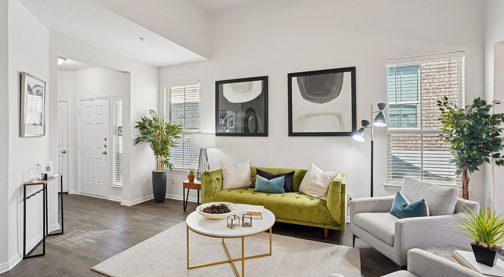 Bright apartment living room with lime-green sofa, gray chairs, plants, and framed art.