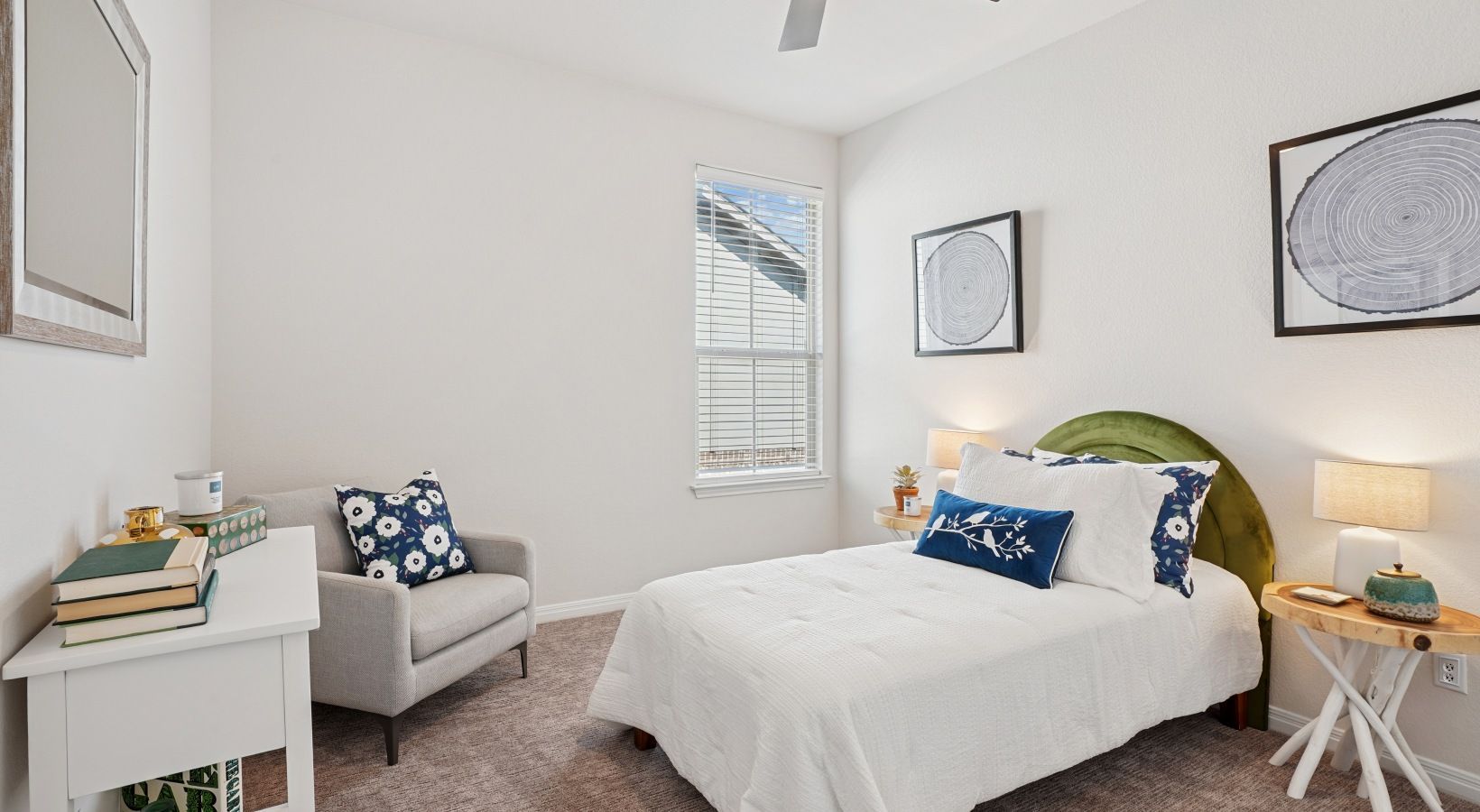 Bedroom inside an apartment featuring white bedding, a green curved headboard, window with blinds, and minimalist decor.