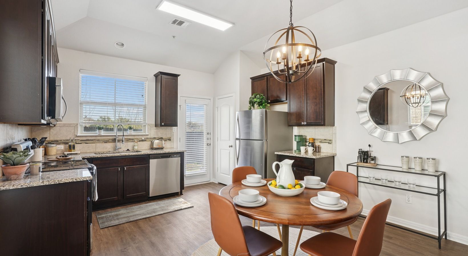Open kitchen with dark wood cabinets, stainless steel appliances, and a round dining table.
