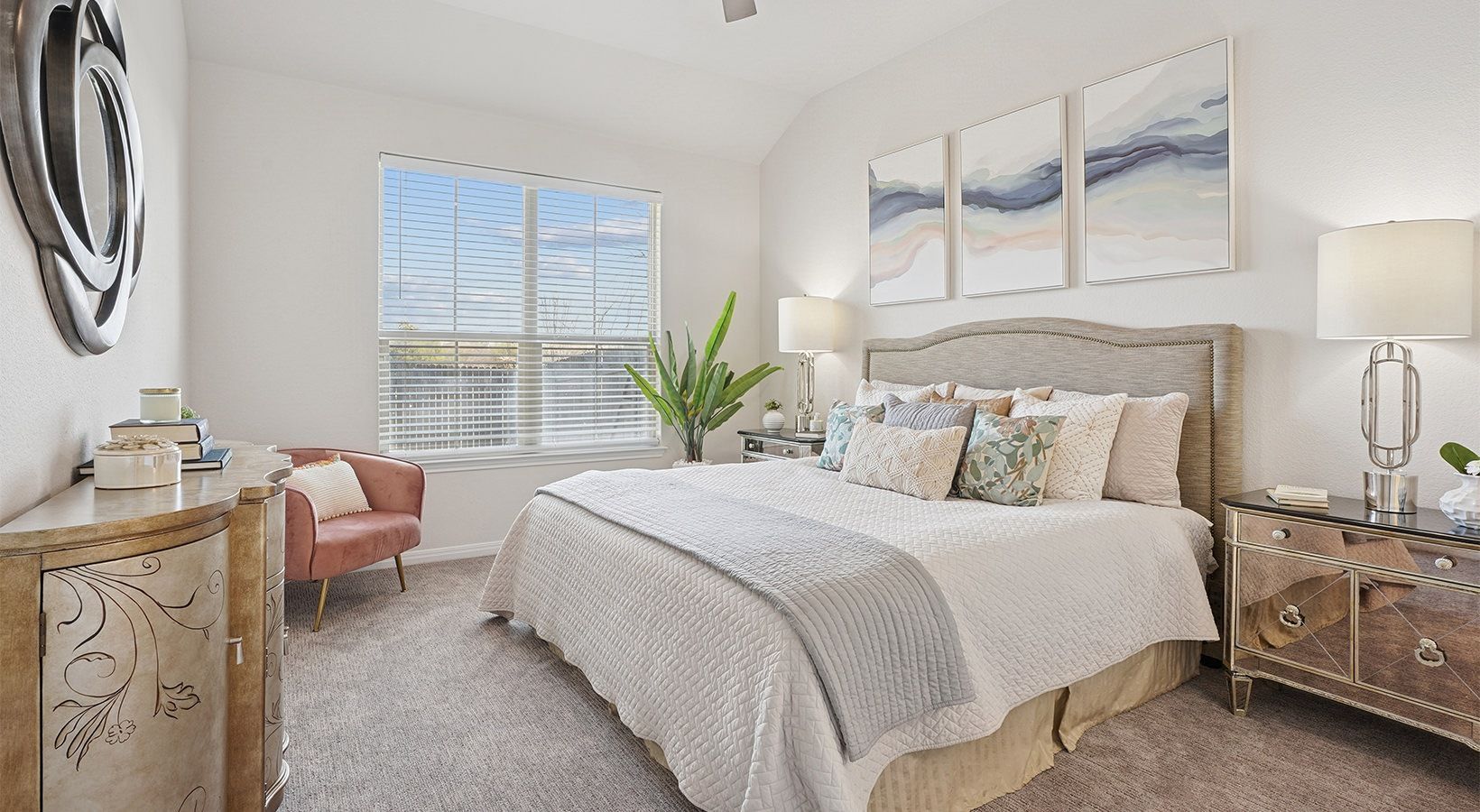 Bedroom in a modern apartment with large bed, nightstands, lamps, plant by window.