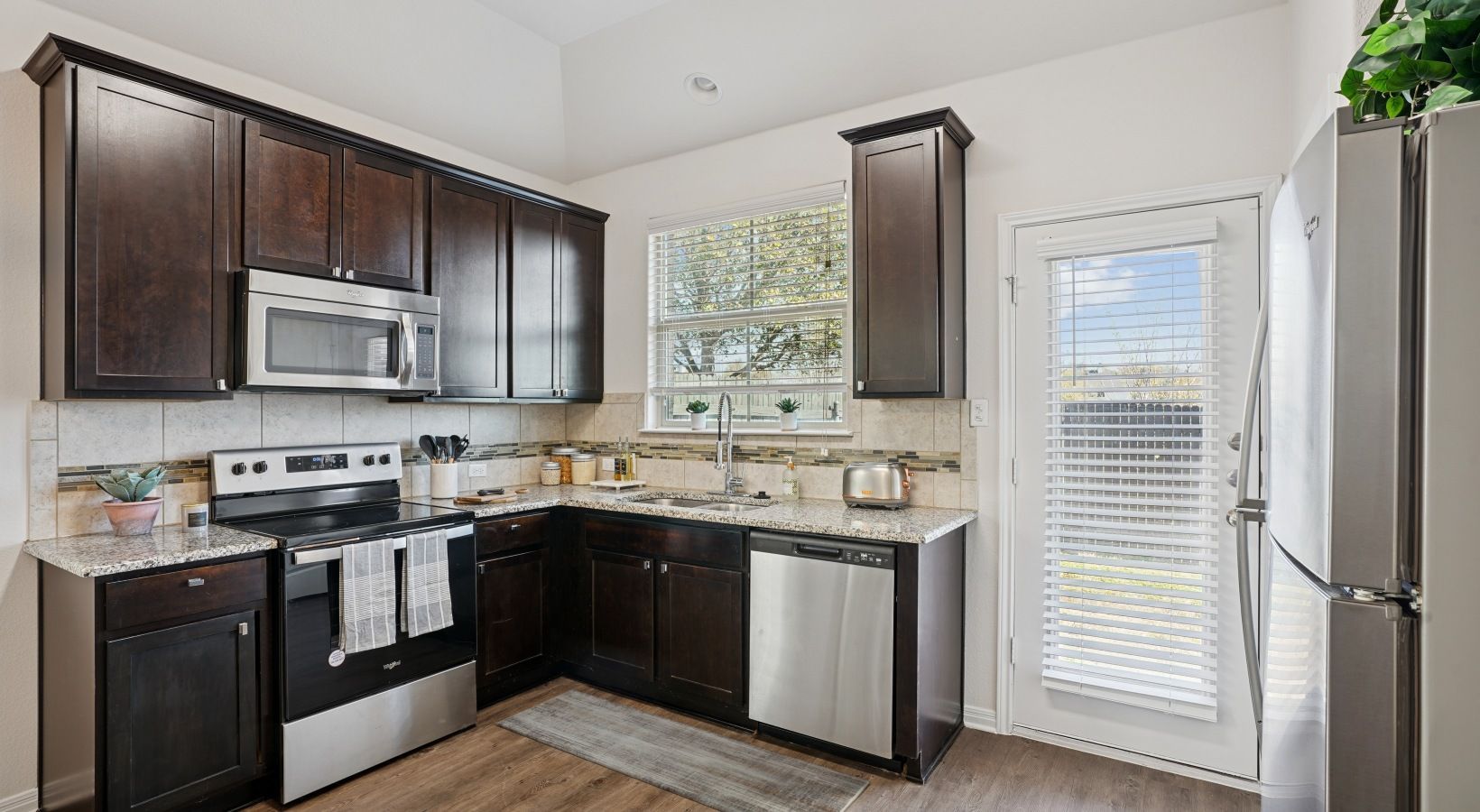 Kitchen in a modern apartment with dark wood cabinets, stainless appliances, and a window above the sink.