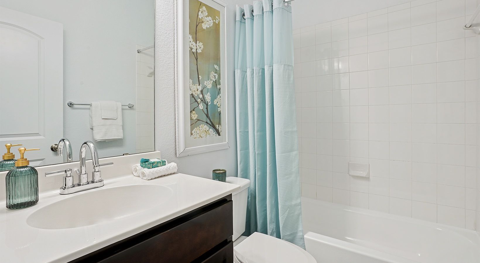 Apartment bathroom with white tile shower, blue shower curtain, and chrome faucet.
