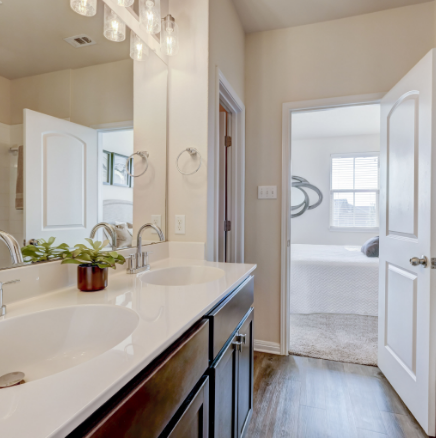 Bathroom with double sinks, mirror, and open doorway to bedroom.