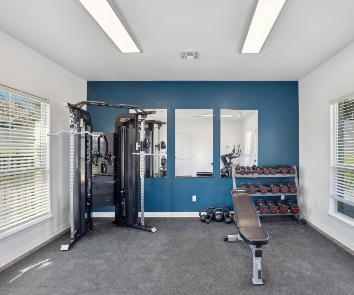 Gym with exercise equipment, including a weight machine, dumbbells, and bench. Teal wall.