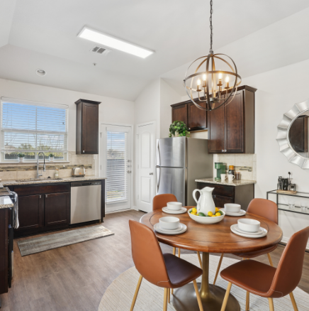 Kitchen with dark cabinets, round table set for four, and stainless steel appliances.