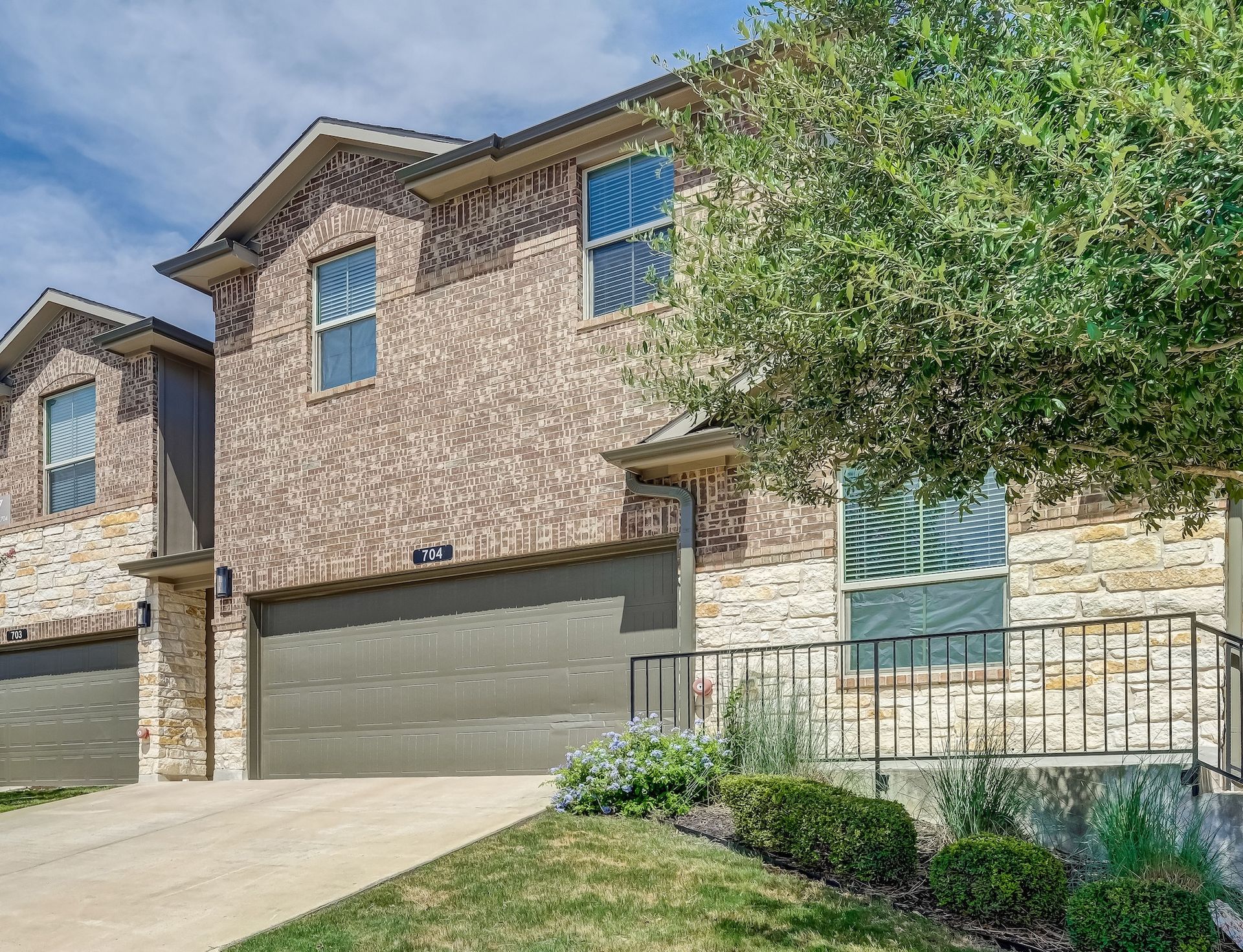 Two-story brick townhomes with attached garages and a small front yard, under a blue sky.